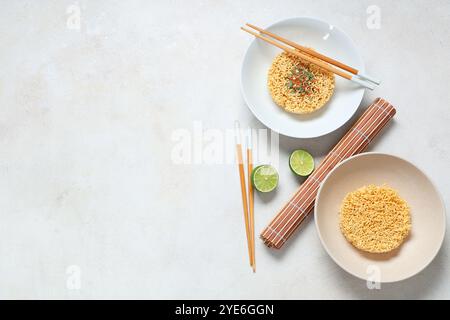 Schüsseln mit rohen Instant-Nudeln, Gewürz, Limette und Holzstäbchen auf weißem Hintergrund Stockfoto