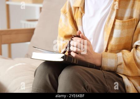 Teenager mit Perlen und Bibel betend auf Sofa zu Hause, Nahaufnahme Stockfoto