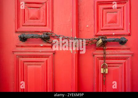 Nahaufnahme von Metallketten und Schlössern in Griffen an rot geschlossenen Türen. Vollformataufnahme des lebendigen Holzeingangs im Freien. Stockfoto