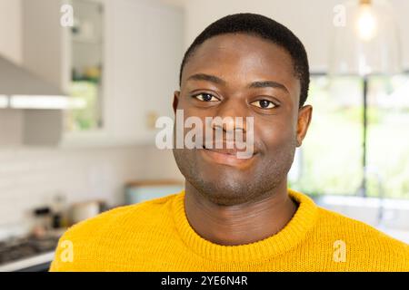 Lächelnder afroamerikanischer Mann in gelbem Pullover, der gemütliche Urlaubsmomente zu Hause genießt Stockfoto