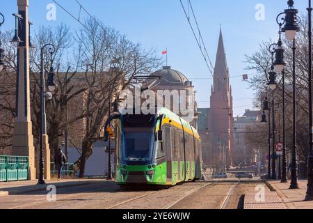 Eine grüne und gelbe Straßenbahn fährt entlang einer Straße in Posen, Polen, mit historischer Architektur und dem hohen Turm der St. Peter-und-Paulus-Kirche im Hintergrund Stockfoto