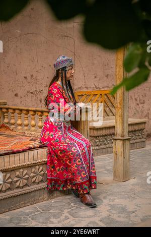 Kashgar, Xinjiang, China - 17. JULI 2023: Ein chinesisches Mädchen in traditioneller uigurischer Kleidung sitzt auf dem Holzsofa in der Straße von Kashgar Ancie Stockfoto