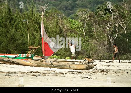 Ein Fischer trägt einen kanister auf der Schulter, während er auf Holzkanus am Tarimbang Beach in Tabundung, East Sumba, East Nusa Tenggara, Indonesien, zuläuft. Stockfoto