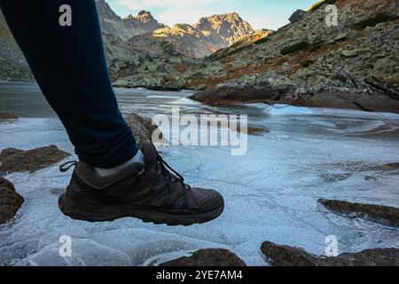 Der Wanderer legt vorsichtig seinen Fuß auf dünnes Eis und bedeckt den Bergsee im malerischen Tal. Stockfoto