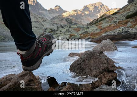 Der Wanderer legt vorsichtig seinen Fuß auf dünnes Eis und bedeckt den Bergsee im malerischen Tal. Stockfoto