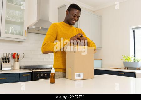 Lächelnder afroamerikanischer Mann im Kücheneröffnungspaket mit ätherischen Ölen, zu Hause Stockfoto