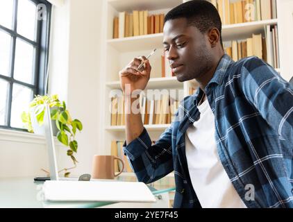 afroamerikaner studiert zu Hause, benutzt Laptop und macht Notizen in einer gemütlichen Bibliothek Stockfoto