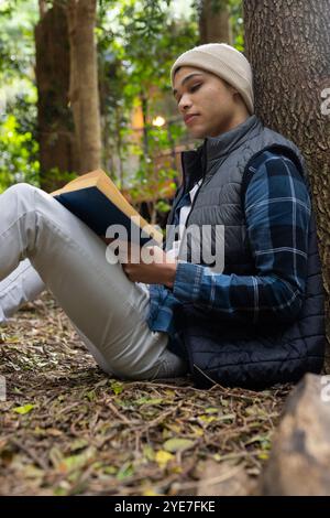 Junger Mann, der draußen Buch liest, sich im friedlichen Wald am Baum entspannt Stockfoto