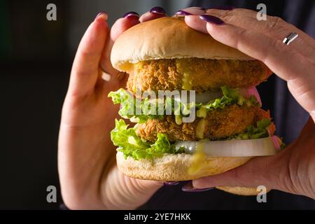 Frau, die Fisch- oder Hühnerburger mit beiden Händen hält Stockfoto