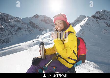 Lächelnde Touristin genießt heißen Tee auf einem sonnendurchfluteten Schneeberg Stockfoto