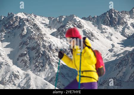 Verschwommene Frau besteigt schneebedeckte Hänge unter hellem Winterlicht in bergigem Gelände Stockfoto