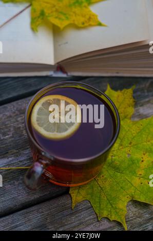 Eine Glasschale heißer Tee mit Zitrone mit Ahornblättern und offenem Buch auf Holzboden. Hochwertige Fotos Stockfoto