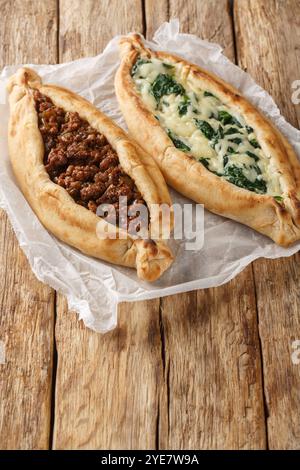 Türkisches Pide-Fladenbrot gefüllt mit Hackfleisch, Käse, Spinat und Kräutern aus nächster Nähe auf Holzbrett auf dem Tisch. Vertikal Stockfoto