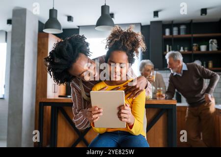 Glückliche afroamerikanische Mutter hilft Teenager-Tochter mit einem digitalen Tablet bei den Hausaufgaben Stockfoto