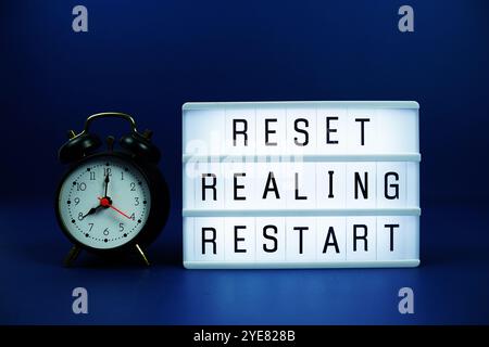 Reset Realing Restart Letterboard Text auf LED Lightbox und Wecker auf blauem Hintergrund Stockfoto