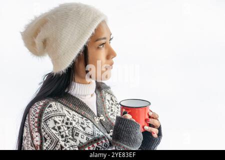 Eine junge Frau in Winterkleidung, die einen Becher in der winterlichen Natur hält, frischer Schnee im Hintergrund Stockfoto