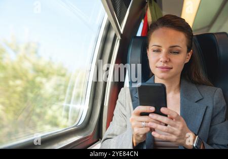 Geschäftsfrau in Geschäftskleidung, die ihr Smartphone benutzt, während sie mit dem Zug reist. Geschäftsreisen und Pendeln Stockfoto