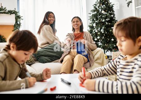 Eine fröhliche Familie verbindet sich beim Stricken und Färben um einen wunderschön geschmückten Weihnachtsbaum. Stockfoto