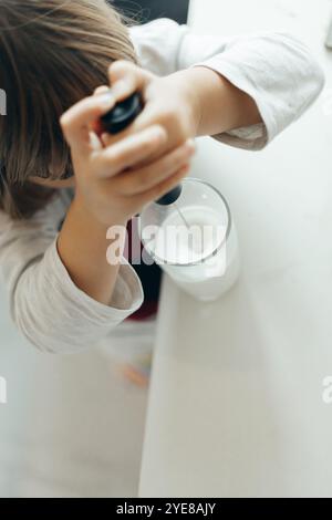 Ein Vorschulkind macht Milchschaum mit einem Handrührgerät in einem Glasbecher in der Küche. Entwicklung von Fertigkeiten im Umgang mit Haushaltsgeräten Stockfoto
