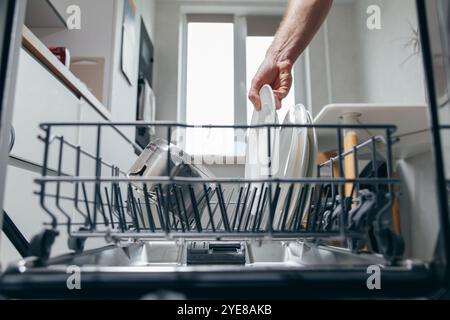 Männliche Hand, die schmutzige Teller in den Geschirrspüler legt, Ansicht von der Innenseite Haushaltsarbeiten, Mann wäscht Geschirr. Stockfoto