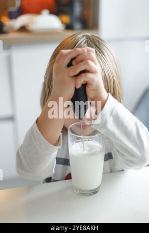 Ein Vorschulkind macht Milchschaum mit einem Handrührgerät in einem Glasbecher in der Küche. Entwicklung von Fertigkeiten im Umgang mit Haushaltsgeräten Stockfoto