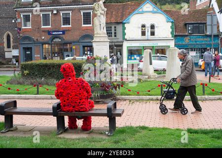 Chesham, Buckinghamshire, Großbritannien. Oktober 2024. Ein älterer Mann geht an einer auffälligen Figur des Mannes vorbei, der mit rotem Mohn bedeckt ist und auf einem Sitz in Chesham neben dem Kriegsdenkmal sitzt und eine weiße Taube hält. Quelle: Maureen McLean/Alamy Live News Stockfoto