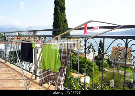 Ein faltbarer Wäscheständer im Freien mit Kleidung und bunten Kleiderschränken, der auf einem Balkon vor dem Hintergrund einer Küstenlandschaft steht Stockfoto
