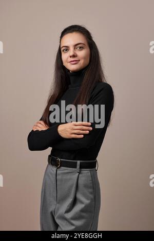 Hübsche Geschäftsfrau mit überkreuzten Armen in schwarzem Pullover isoliert auf grauem Hintergrund Stockfoto