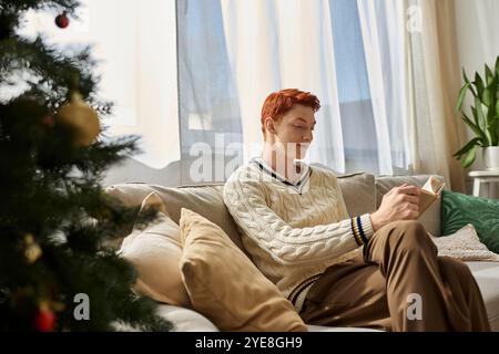 Ein junger Mann sitzt bequem auf einer Couch, in die Lektüre eingetaucht, während ihn festliche Dekorationen umgeben. Stockfoto
