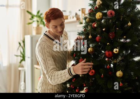 In einem warmen, einladenden Raum schmückt ein junger Mann einen Weihnachtsbaum mit bunten Dekorationen. Stockfoto