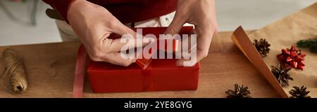 Der junge Mann konzentriert sich darauf, ein Weihnachtsgeschenk mit lebhaften Schleifen und Dekorationen zu verpacken. Stockfoto