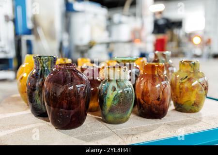 Viele farbenfrohe Glasvasen in der Glasbläserei Fabrik mit Ofenausrüstung auf Hintergrund gesetzt. Handgefertigtes, handgefertigtes Blasglas Stockfoto