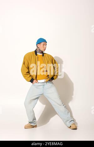 Ein junger Mann mit auffälligen Tätowierungen steht selbstbewusst in einem gelben Pullover und einer Jacke. Stockfoto