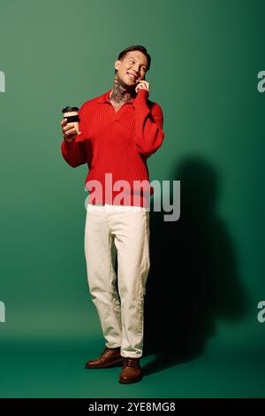 Ein junger Mann mit Tätowierungen steht in einem bunten Raum, hält eine Tasse Kaffee und lächelt hell. Stockfoto