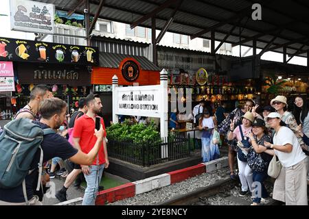 Touristen und Einheimische gehen entlang der Bahngleise, posieren und fotografieren im Handy am Railway Market, Thailand, Mae klong Railway bangkok, Asien Stockfoto