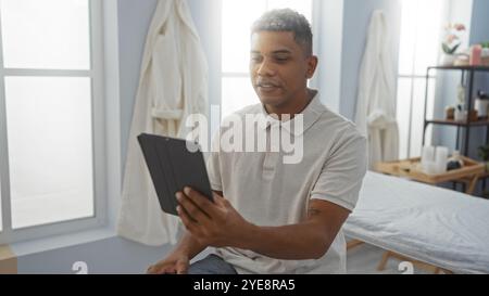 Junger Mann, der ein Selfie mit einer Tablette in einem Reha-Klinikzimmer nimmt, hält einen lässigen Moment drinnen mit einem selbstbewussten Ausdruck in einer medizinischen Umgebung fest. Stockfoto