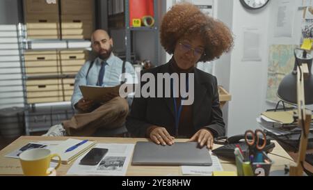 Ein Mann und eine Frau arbeiten als Detektive in einem überladenen Büro mit Beweisakten, einer Karte und einem Laptop. Stockfoto