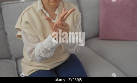 Frau mittleren Alters, die Handgelenkschmerzen hat, während sie drinnen auf einer Couch sitzt Stockfoto