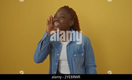 Eine lächelnde junge afroamerikanerin in einer Jeansjacke, die vor einem leuchtend gelben Hintergrund wie schreien Stockfoto