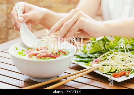Die junge Frau streut Keime zum Pho Bo im vietnamesischen Café Stockfoto