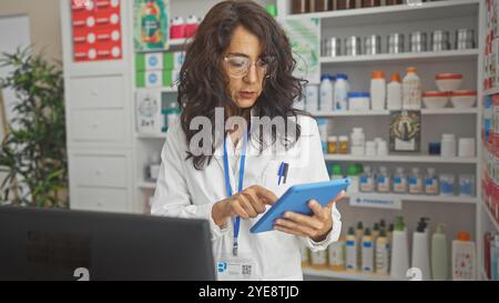 Konzentrierte Apothekerin mittleren Alters, die Medikamenteninformationen auf einer Tablette in einer gut bestückten Apotheke überprüft. Stockfoto