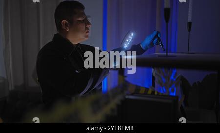Ein konzentrierter hispanischer Mann untersucht einen Tatort drinnen mit einer Lupe und Taschenlampe bei Nacht. Stockfoto