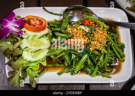 Gebratene Morning Glory mit Sojasauce und Gemüse. Gebratener Wasserspinat auf weißer Platte. Thailändisches Essen. Nahaufnahme, niemand Stockfoto