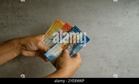 Hand hält schweizer Franken vor einem konkreten Hintergrund und hebt bunte schweizer Banknoten und Finanztransaktionen mit menschlicher Interaktion hervor Stockfoto