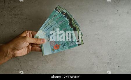 Hand hält malaysische Ringgit-Banknoten vor einem konkreten Hintergrund und fängt die Finger eines Mannes ein, der Geld in malaysia ergreift. Stockfoto