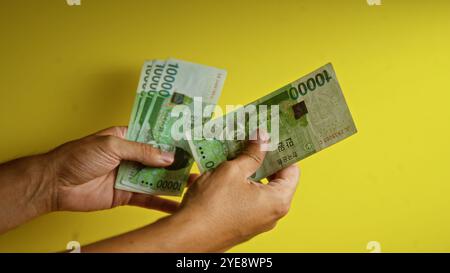 Mann, der südkoreanische Won-Banknoten vor einem leuchtend gelben Hintergrund hält, was die Währungs- und Finanztransaktionen hervorhebt. Stockfoto