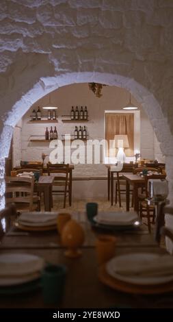 Ein gemütliches italienisches Restaurant im Innenbereich mit rustikaler Einrichtung, Holztischen zum Essen und Weinflaschen auf Regalen vor einer Steinmauer. Stockfoto