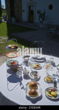 Italienische Frühstücksszene im Freien in apulien mit einem Tisch mit Gebäck, Obst, Tee und verschiedenen Speisen, beleuchtet von der Morgensonne neben einem Restaurant Stockfoto