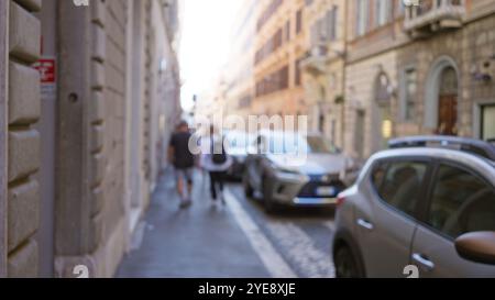 Das unscharfe Bild zeigt ein Paar, das auf einer historischen Straße in rom, italien, spaziert, mit Autos, die nebenan geparkt sind, und einem unscharfen Vintage-Architekturkreat Stockfoto