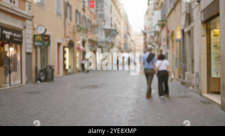 Ein Paar spaziert nachts durch unscharfe Kopfsteinpflasterstraßen roms mit verschwommenen Lichtern im Hintergrund, die das Wesen eines italieners einfangen Stockfoto